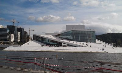Oslo Opera House’s sloping roof rises from the harbor, with visitors walking across its exterior.