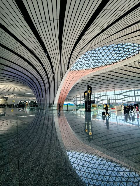 Interior of Beijing Daxing International Airport, showing its sweeping vaulted roof structure and expansive terminal hall.